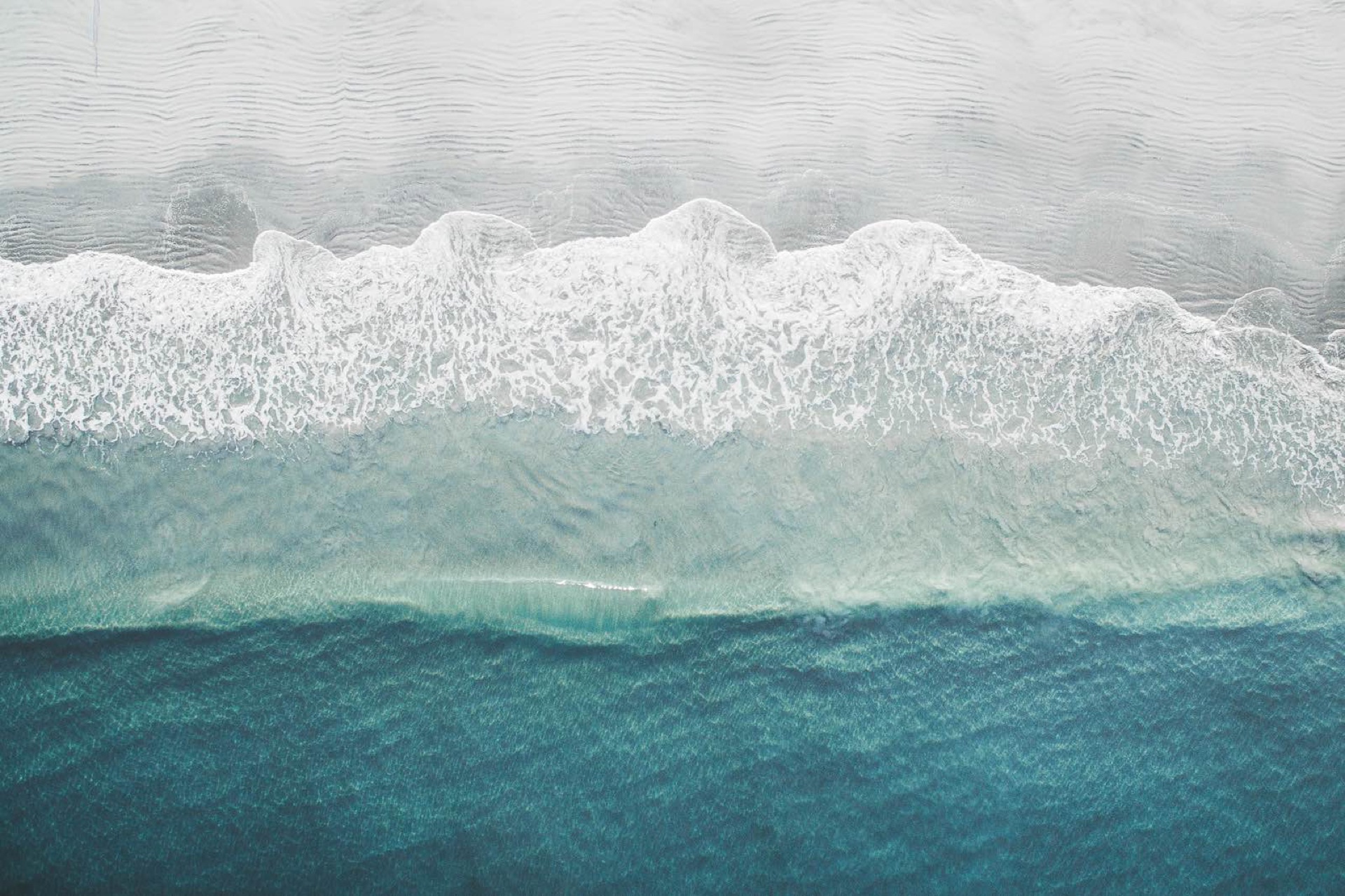 Whitewater rolling onto the North Coast shoreline, seen from above